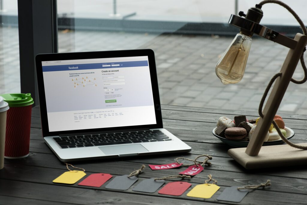 laptop with facebook website on table with macarons, coffee and sale tags in cafe
